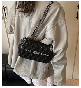 Detailed view of black quilted crossbody bag with silver chain strap on model