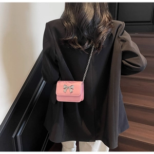 Pink mini chain crossbody bag with silver metal bow shown on model with black suit