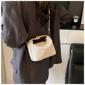 Detail of cream woven pillow bag with gold clasp worn over a grey oversized blazer