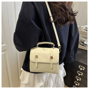 Detail of cream crossbody bag shown on model highlighting size and gold buckle design