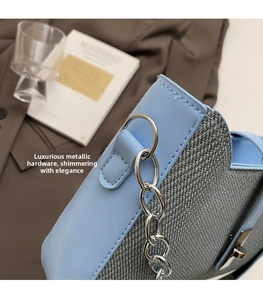 Primer plano del bolso de cuero azul y tela gris con cadena de anillos plateados y costuras