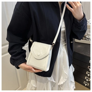 Detailed view of a white quilted crossbody phone bag worn over a black jacket