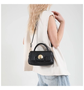 Detail of black leather crossbody bag with iconic gold circular metal buckle and strap