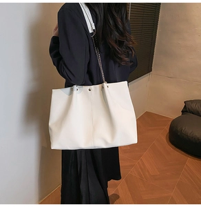 Detailed view of white tote bag with vertical stitching and gold stud accents