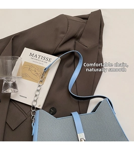 Detalle de bolso bandolera azul claro texturizado con cadena plateada y hebilla de cuero