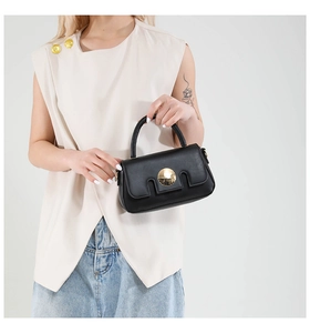 Detail of a minimalist black leather handbag with a gold round buckle and U-shaped flap
