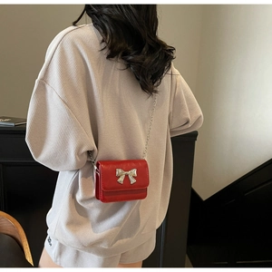 Close-up of red leather mini crossbody bag with silver bow buckle worn on chain