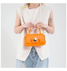 Detail of orange leather handbag showing golden round lock and U-shaped cutout design