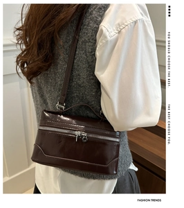 Close-up of a glossy dark brown patent leather box bag worn by a model in a minimal setting