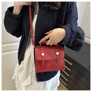 Detail of a vintage dark red square handbag with gold buckles worn as a crossbody bag
