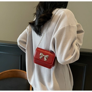 Detail of red glossy crossbody bag with silver bow accent and chain strap worn by a model