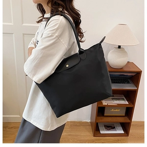 Grand sac cabas en nylon noir avec anses en cuir porté par un mannequin en intérieur