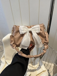 Detail of coffee brown ruched handbag featuring a large white organza bow and chain strap