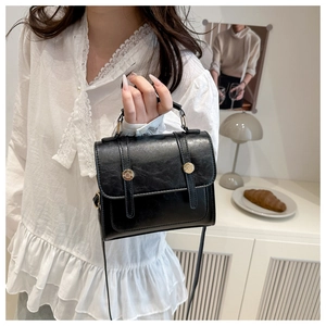 Detail of a black textured leather handbag featuring a golden buckle and top handle