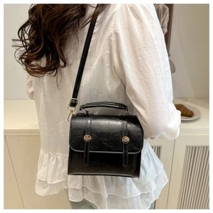 Black textured leather square handbag with silver metal buckles worn cross-body by a model