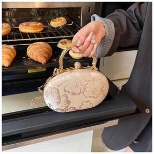 Close-up of champagne satin evening bag with floral embroidery and golden metal handle