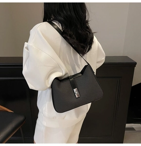 Detail of black minimalist underarm bag featuring a textured finish and silver rotary lock