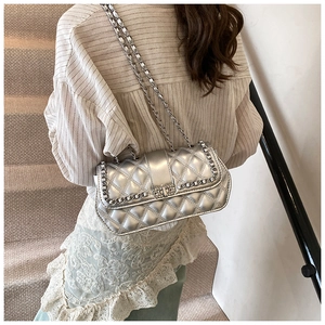 Detail of silver quilted flap bag showing metal chain strap on a model's shoulder