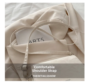 Detail view of the adjustable cream white shoulder strap on a sleek faux leather saddle bag