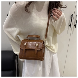 Lifestyle shot of a brown structured faux leather crossbody bag with gold hardware