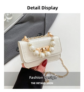 Détail d'un sac à main blanc à motif crocodile avec poignée en perles et chaîne dorée