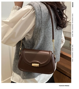 Detail of dark brown leather handbag featuring a golden cylindrical lock and metal chain