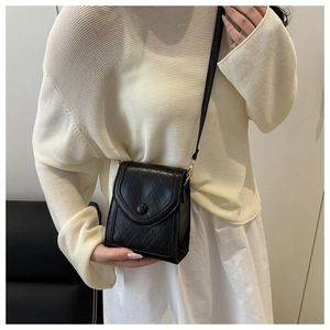 Detail of black quilted crossbody bag with round buckle and fine shoulder strap