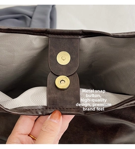 Detail of golden cylindrical magnetic closure on a brown leather tote with herringbone lining