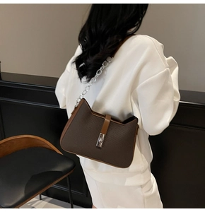 Detail of dark brown embossed leather shoulder bag with silver twist lock on female model