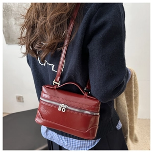 Detailed view of dark red leather box crossbody bag worn over a blue sweater