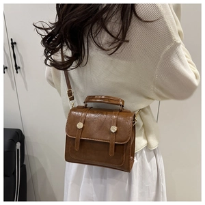 Close-up of brown faux leather mini square bag with gold buckles and adjustable strap