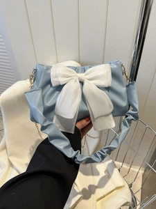 Close-up of light blue pleated handbag with large white organza bow and gold chain strap