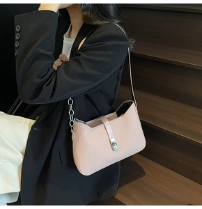 Detail of light pink chevron textured underarm bag with metallic buckle on black suit