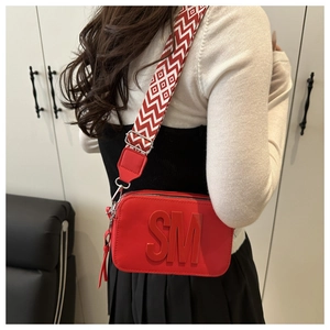 Dettaglio della borsa rossa con logo a rilievo e tracolla larga a motivi geometrici