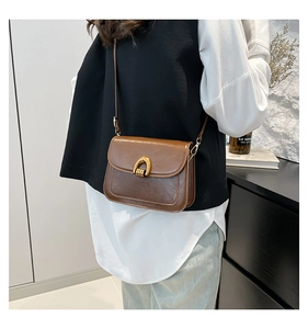 Close-up of brown vintage saddle bag with U-shaped gold buckle worn over the shoulder