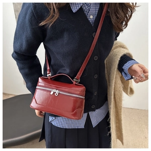 Detail of dark red rectangular box bag with glossy finish and silver double zippers