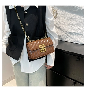 Detail of a brown quilted patent leather crossbody bag featuring a gold chain and geometric clasp