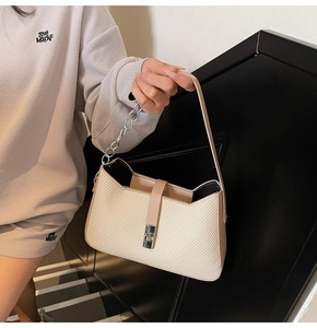 Close-up of cream woven shoulder bag featuring a silver twist lock and chain strap detail