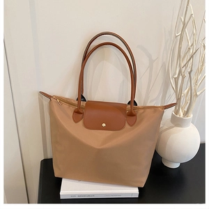 Détail du sac cabas en nylon kaki avec anses en cuir marron et bouton doré sur un livre blanc