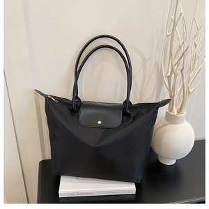 Détail du sac cabas en nylon noir avec poignées en cuir, rabat à pression et zip doré