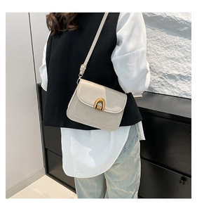Detailed side view of cream white saddle bag with golden horseshoe clasp worn by a model