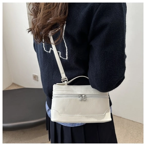 Detail view of a cream white square crossbody bag with silver zippers on a model