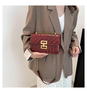 Detail of burgundy patent leather crossbody bag with gold chain and metal buckle