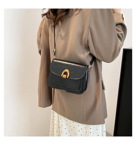 Detail of black oil wax leather saddle bag with gold U-shaped buckle on female model