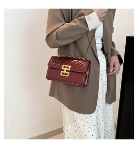 Detail of burgundy crossbody bag with V-shaped quilting and gold metal lock on a model