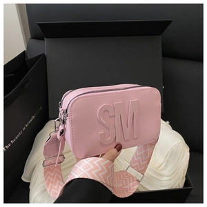 Dettaglio della borsa rosa con lettere a rilievo e tracolla geometrica larga
