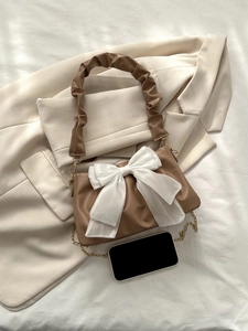 Detail of brown pleated handbag with a large white organza bow and golden chain strap