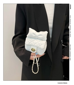Close-up of white quilted mini crossbody bag with a large decorative bow and gold chain