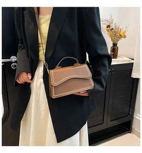 Detail of caramel brown handbag with white decorative stitching and wavy flap design