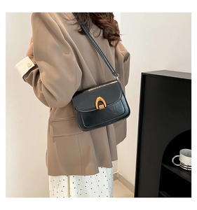 Detail shot of a black oil wax leather saddle bag with golden horseshoe buckle on a model